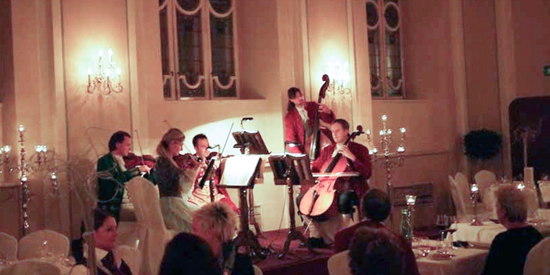 Kammermusikensemble in historischen Kostümen bei einem Barockkonzert in festlichem Saal mit Kerzenlicht.
